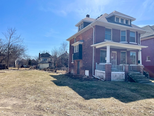 view of side of property with brick siding, covered porch, a chimney, and a lawn