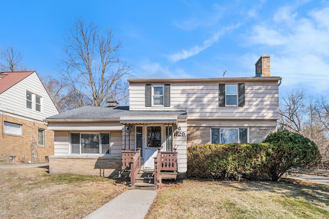 view of front facade with a front yard, brick siding, and a chimney