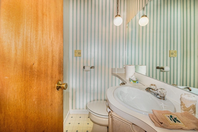 bathroom with tile patterned floors, wallpapered walls, toilet, and vanity