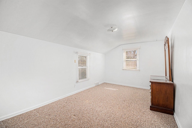 empty room featuring lofted ceiling, light colored carpet, and baseboards