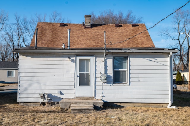 back of house with a lawn, a chimney, and a shingled roof