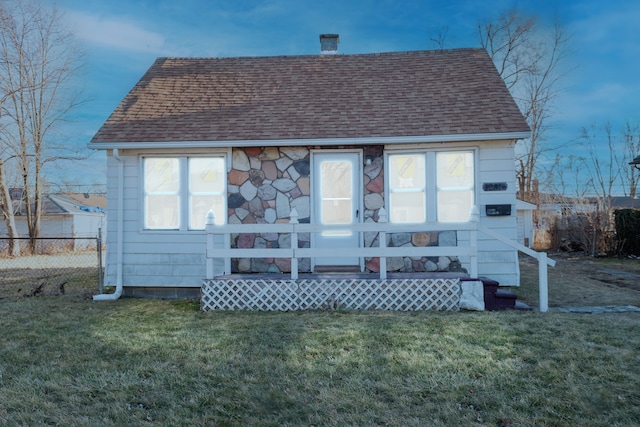 back of property featuring fence, a shingled roof, a chimney, stone siding, and a lawn