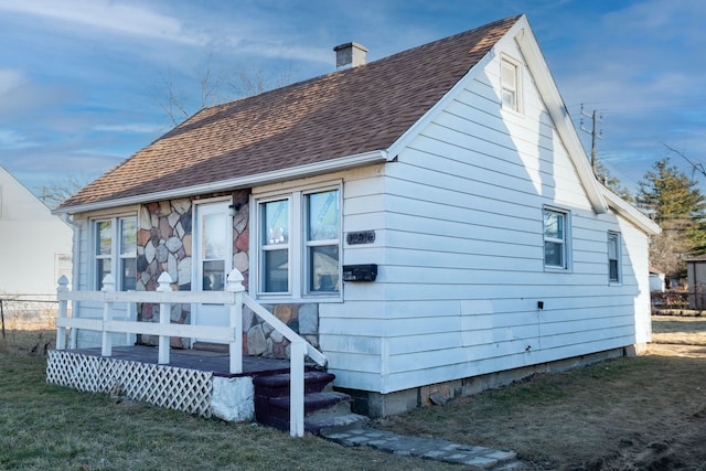 back of property featuring a lawn, a chimney, and a shingled roof