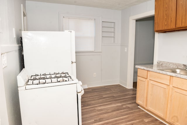 kitchen with light brown cabinetry, light countertops, wood finished floors, white appliances, and a sink