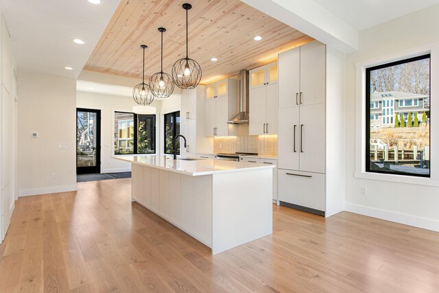1 N Bailey Ave # 1, South Haven, MI 49090 - kitchen with wooden ceiling, wall chimney range hood, light wood-style flooring, an island with sink, and light countertops
