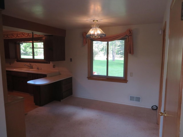 kitchen featuring visible vents, light colored carpet, a peninsula, an inviting chandelier, and a sink