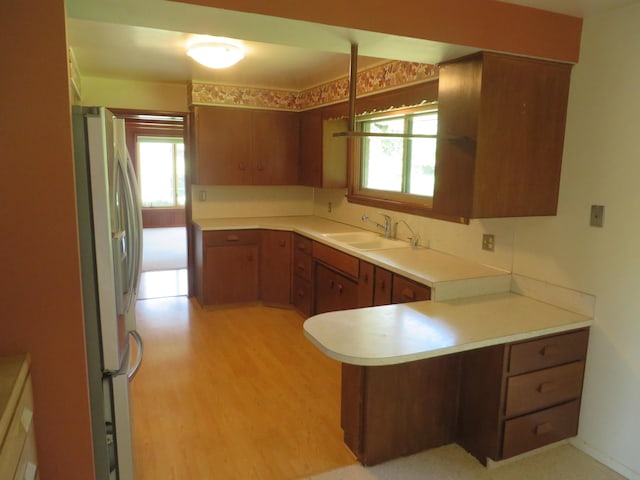 kitchen with brown cabinetry, a peninsula, freestanding refrigerator, a sink, and light countertops