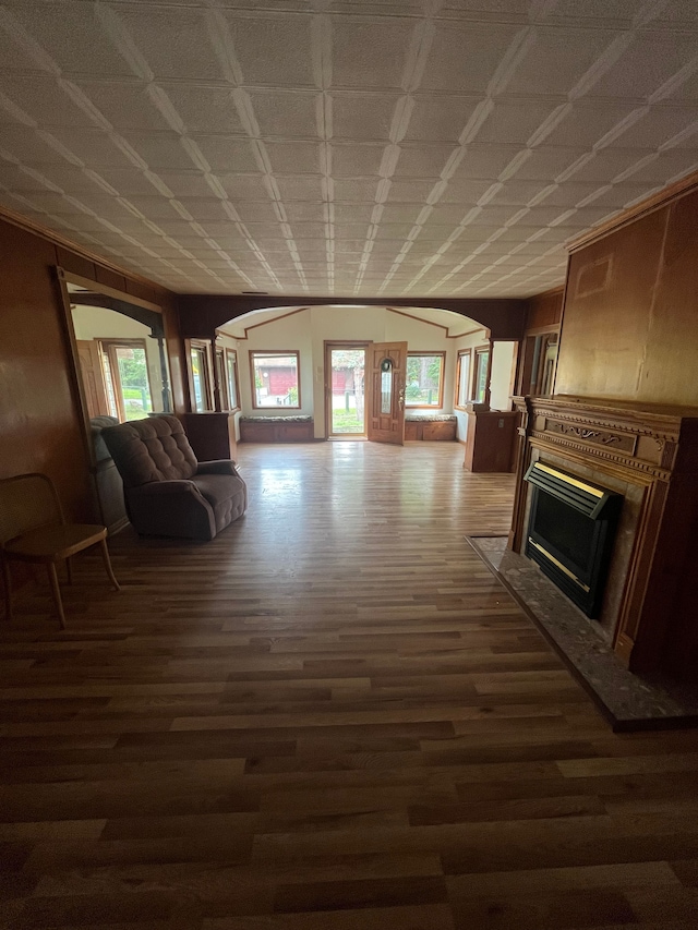 unfurnished living room featuring arched walkways, plenty of natural light, wood finished floors, and a fireplace