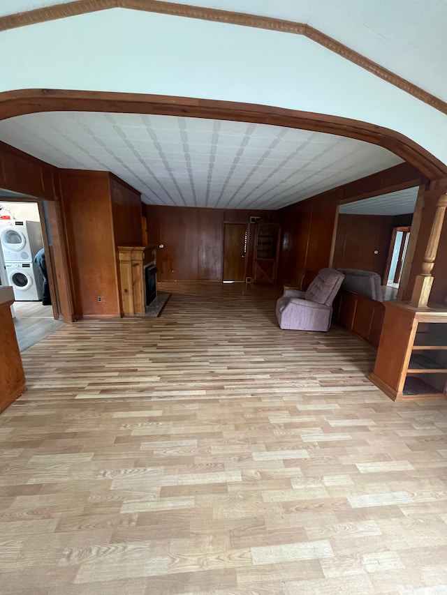 unfurnished living room with lofted ceiling, light wood-style flooring, washer / clothes dryer, arched walkways, and wood walls