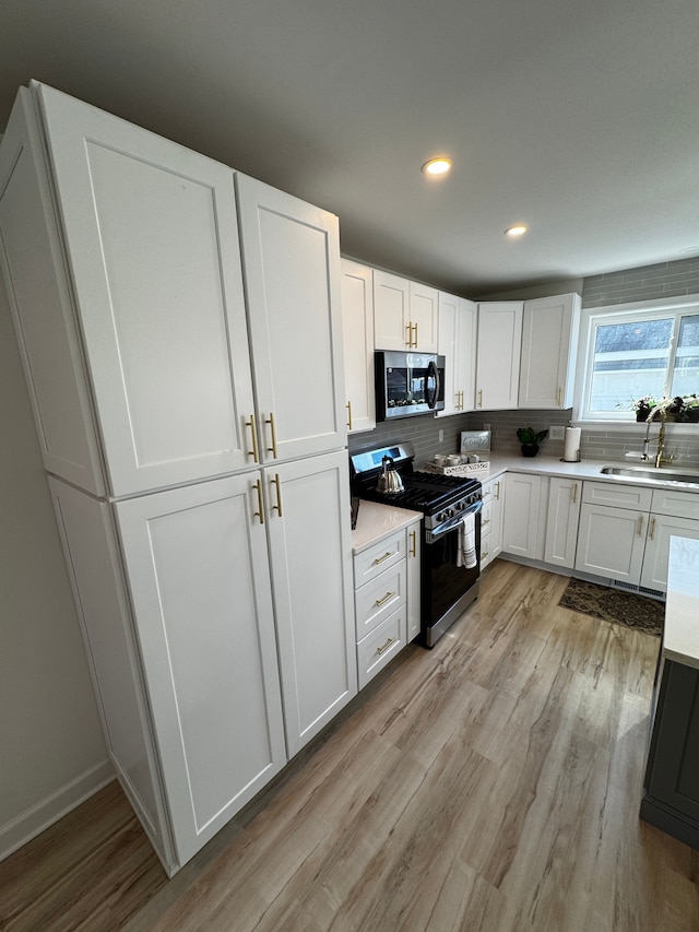 kitchen featuring light wood finished floors, a sink, light countertops, appliances with stainless steel finishes, and white cabinetry