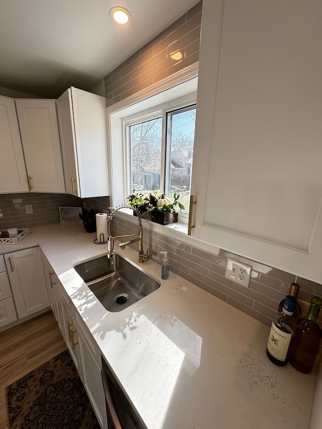 kitchen with backsplash, white cabinets, light stone countertops, and a sink