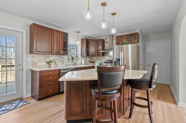 kitchen featuring a sink, wall chimney range hood, stainless steel appliances, light countertops, and decorative backsplash