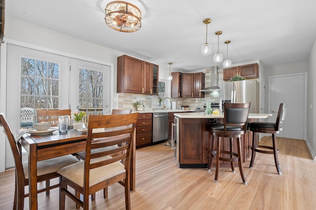 kitchen featuring wall chimney range hood, appliances with stainless steel finishes, light wood finished floors, decorative backsplash, and light countertops