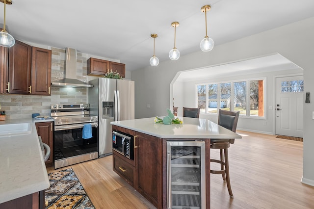 kitchen with tasteful backsplash, stainless steel appliances, wine cooler, light wood-style floors, and wall chimney exhaust hood