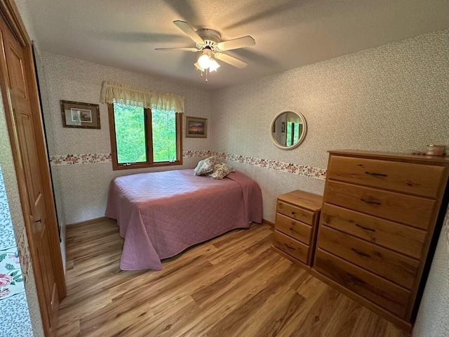 bedroom featuring light wood-style flooring, wallpapered walls, and a ceiling fan