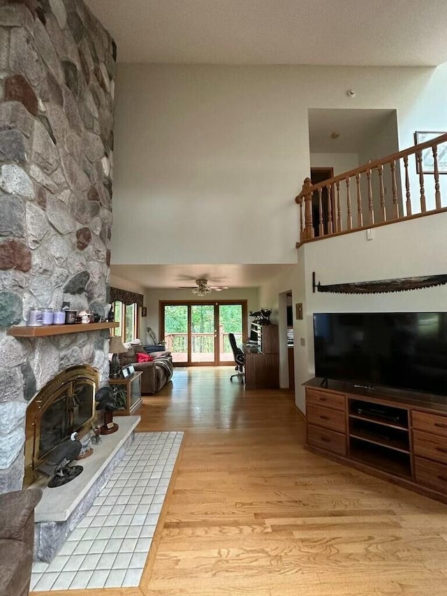 living room featuring a fireplace, a ceiling fan, a high ceiling, and light wood-style floors