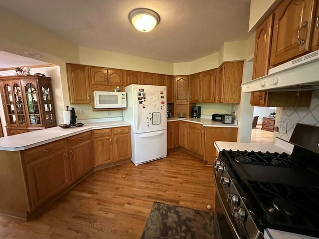 kitchen featuring under cabinet range hood, light countertops, brown cabinets, wood finished floors, and white appliances