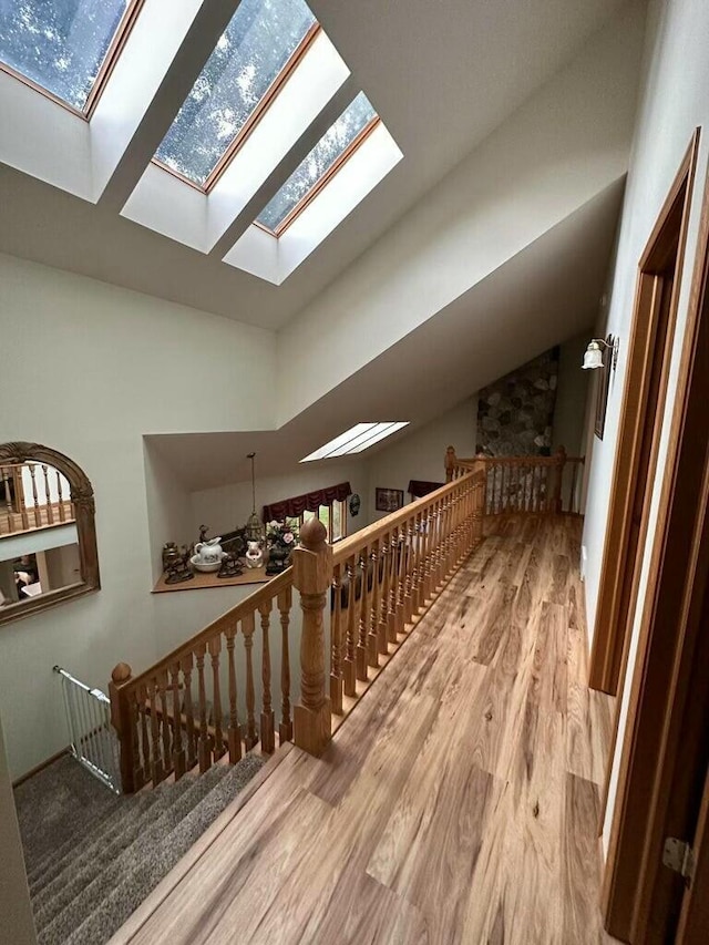 hall with wood finished floors, vaulted ceiling with skylight, and an upstairs landing