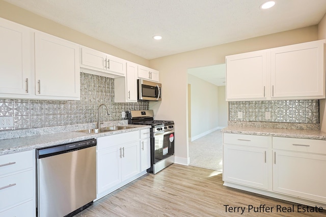 kitchen with a sink, light wood-style floors, appliances with stainless steel finishes, and white cabinets