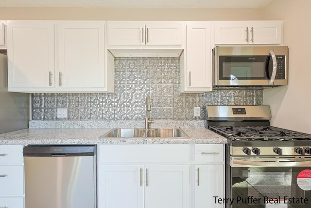 kitchen featuring light stone counters, a sink, decorative backsplash, appliances with stainless steel finishes, and white cabinetry