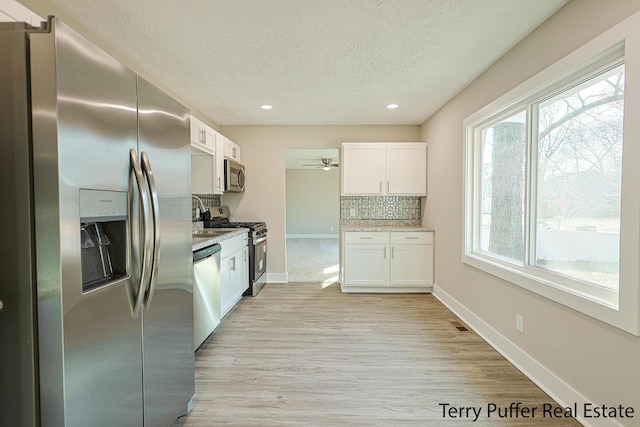 kitchen featuring light wood finished floors, stainless steel appliances, decorative backsplash, white cabinets, and a textured ceiling