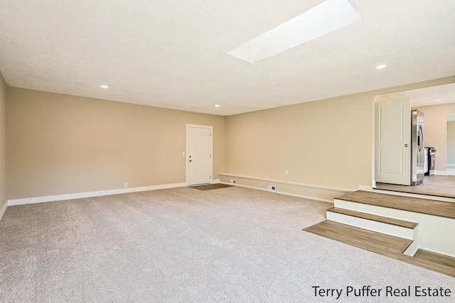 spare room featuring a textured ceiling, a skylight, and carpet floors