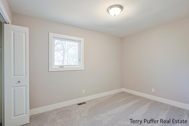 carpeted empty room with baseboards, visible vents, and a textured ceiling