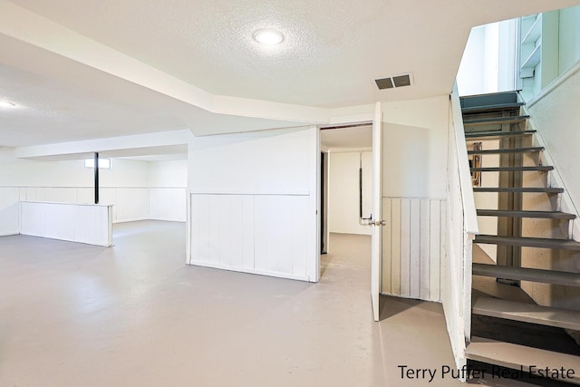 basement featuring stairway, wainscoting, visible vents, and a textured ceiling