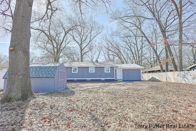 back of house with an outbuilding, fence, a shed, a shingled roof, and crawl space