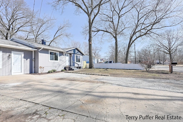 view of property exterior featuring concrete driveway, a chimney, and fence