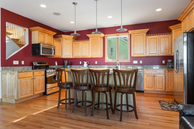 kitchen with light wood-style flooring, light brown cabinetry, recessed lighting, appliances with stainless steel finishes, and a breakfast bar area