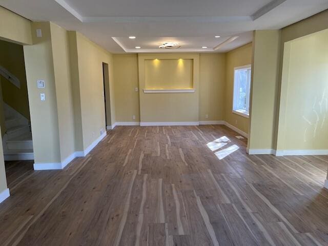 unfurnished room featuring wood finished floors, baseboards, a tray ceiling, recessed lighting, and stairs