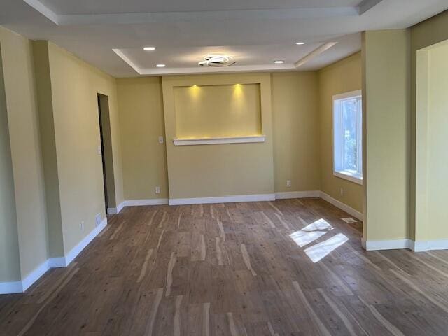 unfurnished room featuring recessed lighting, a raised ceiling, baseboards, and wood finished floors