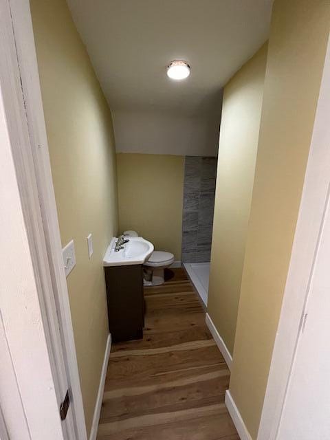 bathroom with baseboards, toilet, tiled shower, wood finished floors, and a sink