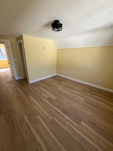 empty room with lofted ceiling, wood finished floors, and baseboards