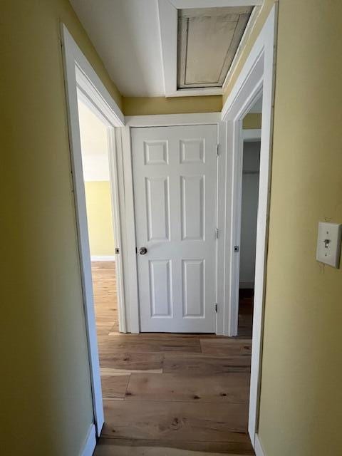 hall featuring baseboards, attic access, and wood finished floors