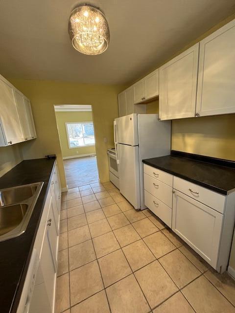 kitchen with a sink, dark countertops, white appliances, white cabinets, and light tile patterned floors