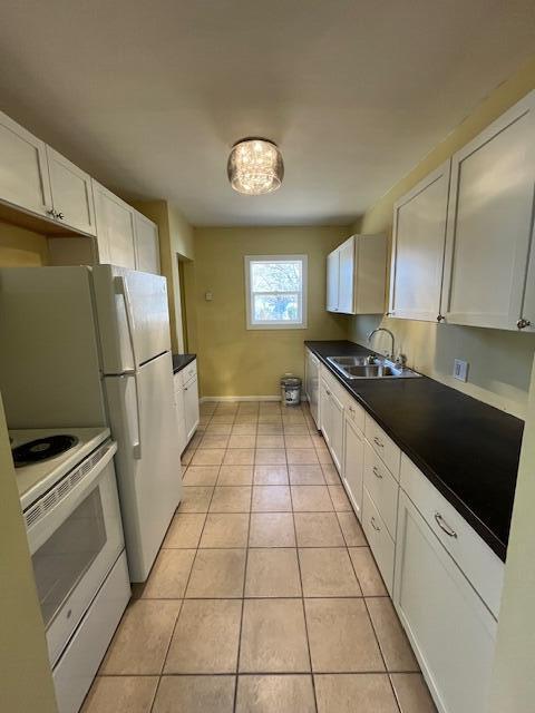 kitchen featuring dark countertops, light tile patterned floors, white appliances, white cabinetry, and a sink