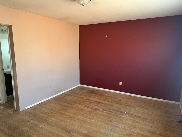 unfurnished room featuring hardwood / wood-style floors, baseboards, and a sink