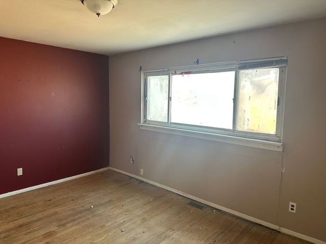 empty room featuring hardwood / wood-style floors, visible vents, and baseboards