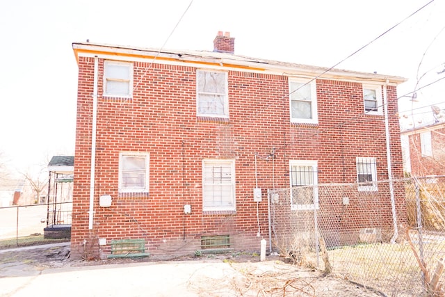 back of house featuring brick siding, a chimney, and fence