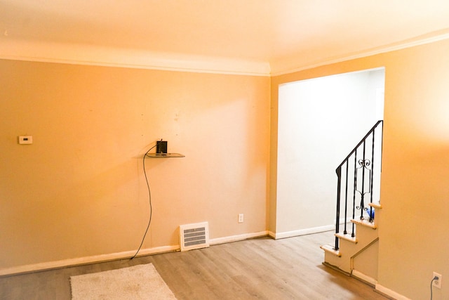 empty room featuring stairway, wood finished floors, baseboards, visible vents, and ornamental molding