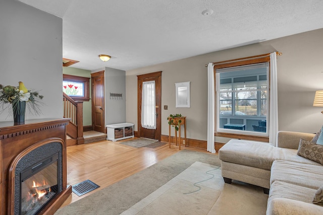 living room with visible vents, baseboards, stairs, light wood-type flooring, and a glass covered fireplace