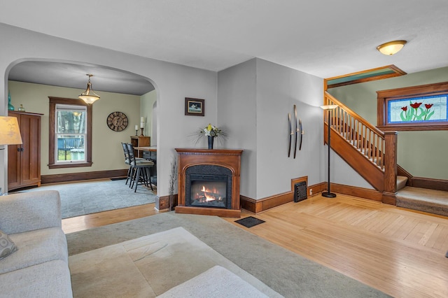 living room featuring a glass covered fireplace, stairs, wood finished floors, and plenty of natural light