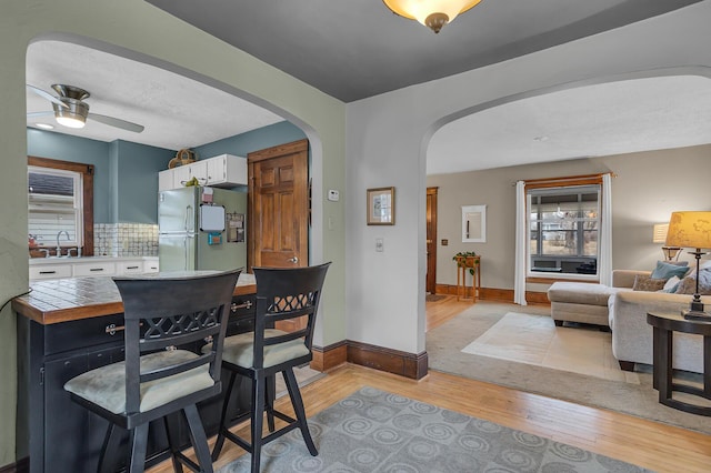 dining space with baseboards, arched walkways, light wood-style floors, and a ceiling fan