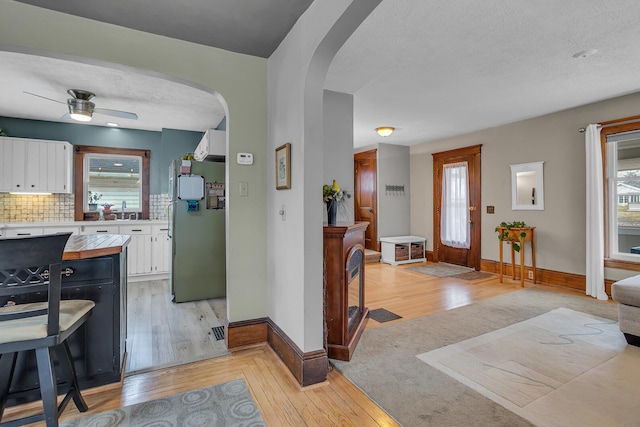 interior space featuring baseboards, light wood-style flooring, arched walkways, a textured ceiling, and a ceiling fan