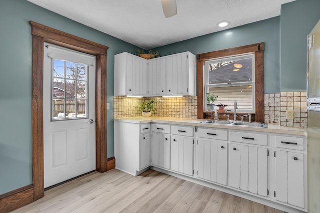 kitchen with a sink, white cabinetry, light wood-style flooring, and light countertops