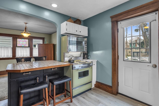 kitchen featuring stainless steel microwave, electric stove, light wood-style floors, arched walkways, and white cabinets