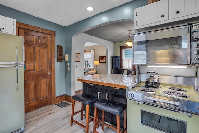 kitchen featuring stainless steel microwave, electric range oven, freestanding refrigerator, arched walkways, and white cabinetry