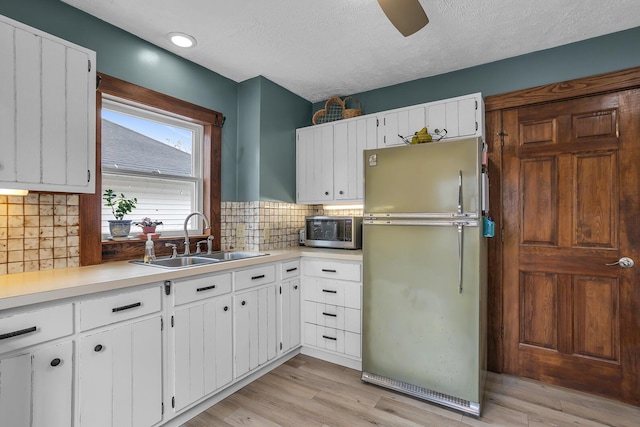 kitchen featuring freestanding refrigerator, a sink, light countertops, light wood-style floors, and stainless steel microwave